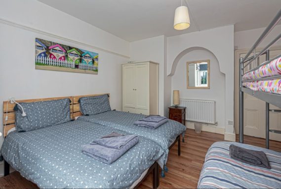 A modern bedroom with two beds, a bunk bed, and colourful wall art.
