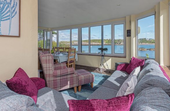 Bright coastal living area with large windows, inviting seating, and scenic water views.