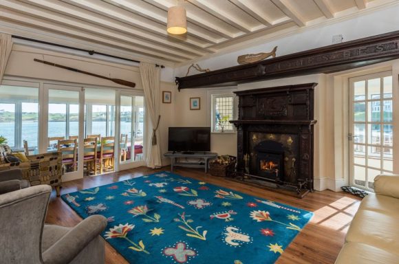 Bright living room with a large rug, fireplace, and views of the water through glass doors.