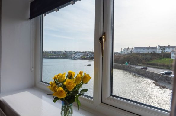 A vase of yellow flowers by a window overlooking a scenic coastal view.