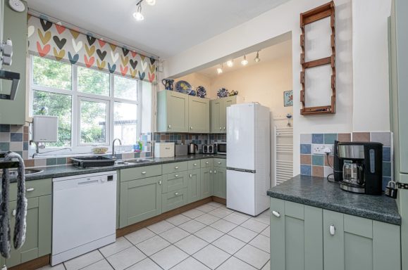 Bright kitchen with green cabinets, white appliances, and a patterned curtain.