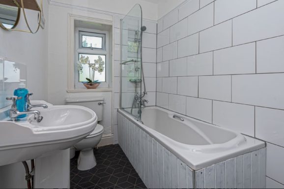 Bright bathroom featuring a bathtub, sink, and modern glass shower screen against tiled walls.