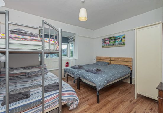 A bright, tidy bedroom with a bunk bed and a double bed, featuring wooden flooring.