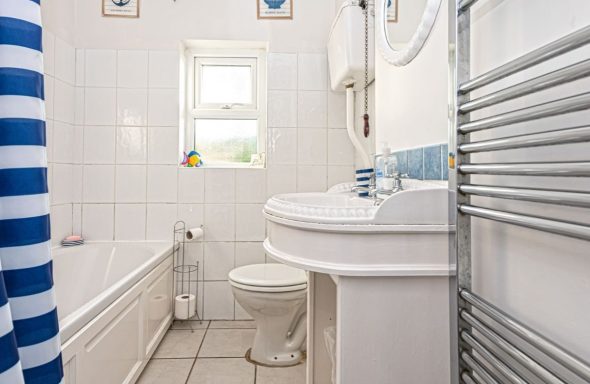 Bright bathroom with a bath, sink, and striped shower curtain, featuring a towel radiator.