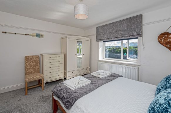Bright bedroom with a double bed, wardrobe, and chair, featuring grey decor and natural light.