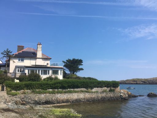 Coastal house with a garden beside a calm sea and blue sky.