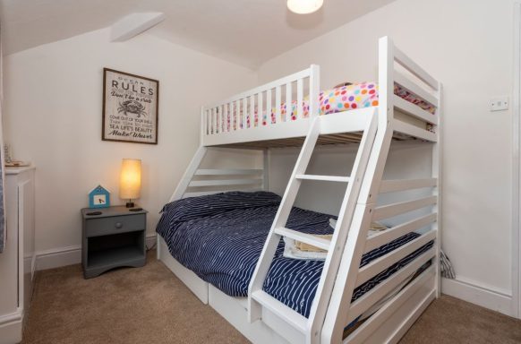 A bedroom featuring a white bunk bed with blue bedding and a bedside table.
